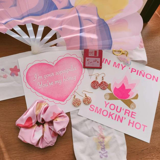 assortment of pink items - folding fan inspired by Sandia mountains, acrylic keychain of same design, floppy disk wooden pin, laser cut earrings (hand painted, hand assembled), risograph printed valentines, star print scrunchie, star print over-knee stocki